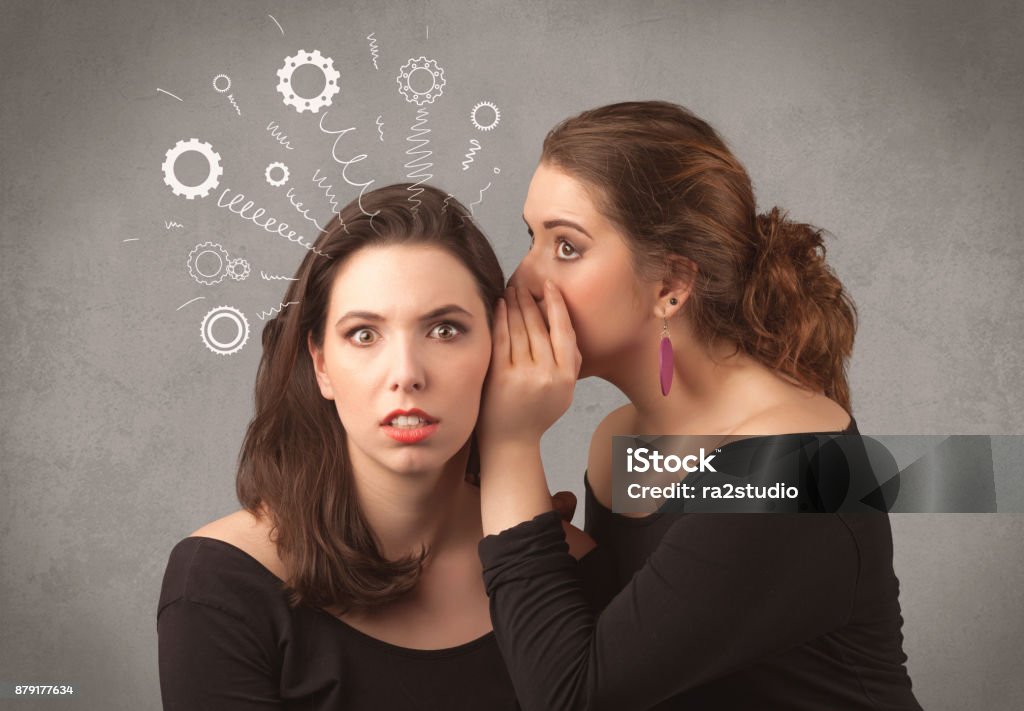 girl telling secret things to her girlfriend Two girlfriends in elegant black dress sharing secrets with each other concept with drawn rack cog wheels and spiral lines on the wall background. Actress Stock Photo
