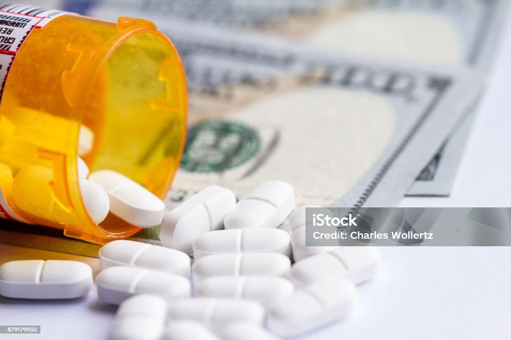 Opioid pain killers close up of a prescription bottle with white tables falling out on top of a group of hundred dollar bills Price Stock Photo