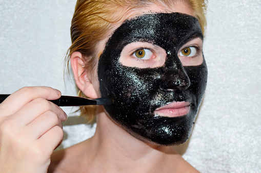 Niña en una máscara negra cosmética. Máscara de limpiamiento de la aspirina y el carbón activado. Mascarilla facial cosmético negro. photo