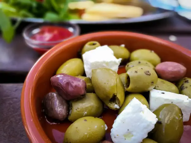 Photo of Overhead view of selection of black and green olives with feta cheese in terracotta dish