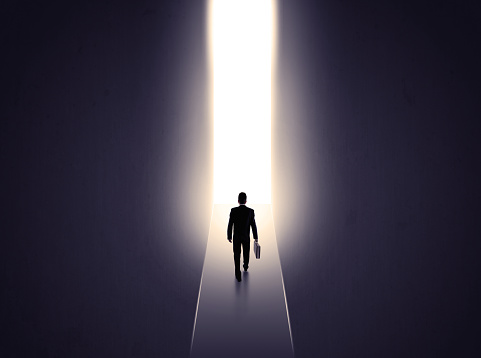 Young businessman stands in dark tunnel and looks in the glowing end