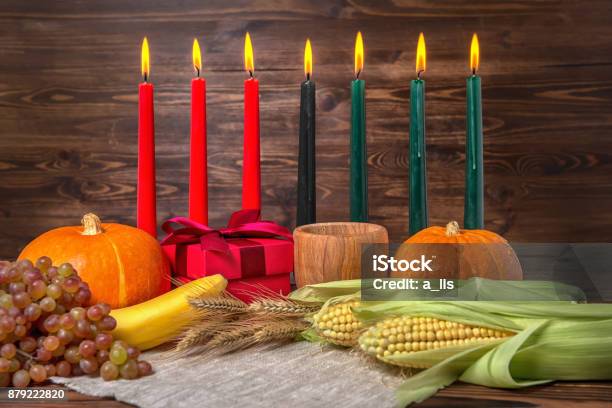 Kwanzaa Festival Concept With Seven Candles Red Black And Green Gift Box Pumpkins Ears Of Wheat Grapes Corns Banana Bowl And Fruits On Wooden Background Close Up Stock Photo - Download Image Now