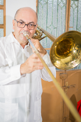 Slide trombone player while rehearsing in his room. Not a pretty background but this image can be worked according to clients particular needs. The player is sharp and well illuminated.