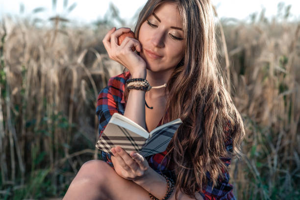 domaine de belle fille étudiante. dans sa pomme de la main. nouvelles idées de concept, à l’extérieur, l’été dans la nature. dans carnet de main, cheveux longs. idées intelligentes. inspiration de créativité. lit le journal. - paper document pen long hair photos et images de collection