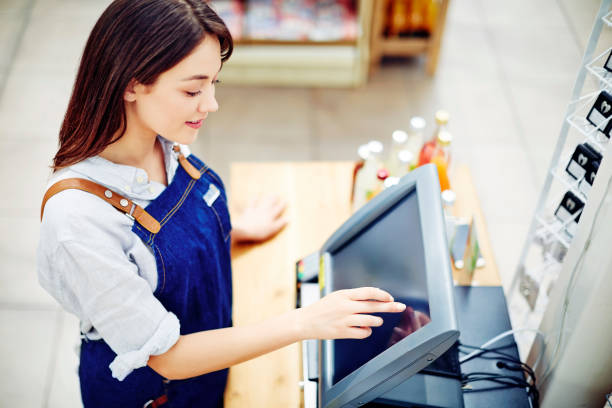 Young female deli owner using cash register in store