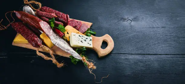 Assortment of cheeses and traditional sausages on a wooden background. Brie cheese, blue cheese, gorgonzola, fuete, salami. Free space for text. Top view.