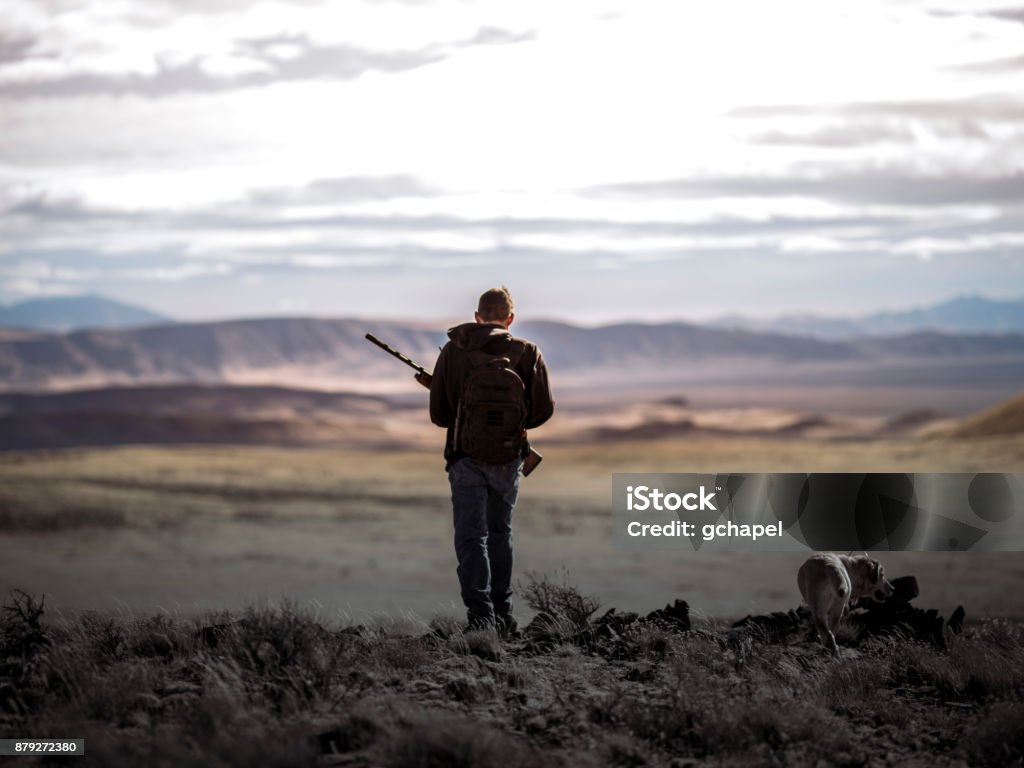 Chasseur de millénaire avec un chien de chasse Labrador jaune marchant dans le désert du Nevada accidenté. - Photo de Type de chasse libre de droits