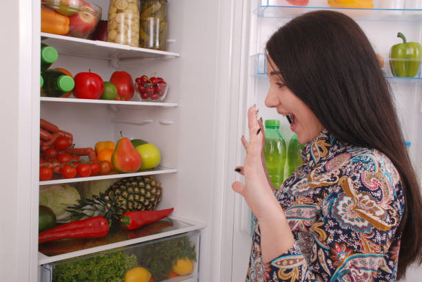 istock Young girl with an amused face on the refrigerator background 879276056