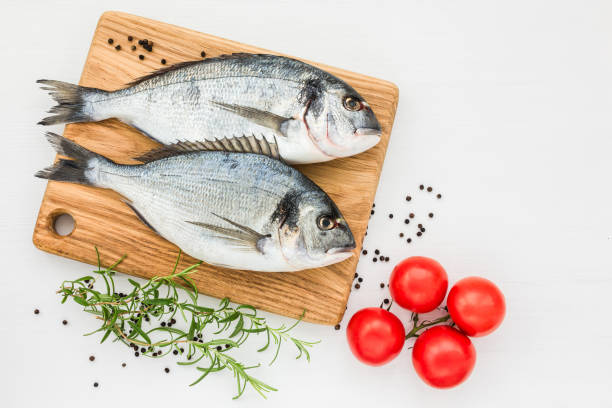 istock Fresh dorado fish on wooden cutting board with tomatoes on white table. Top view, copy space. 879298606