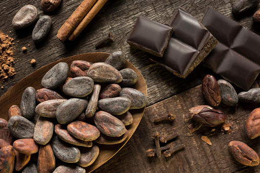 Cocoa and cinnamon composition on wooden surface, showing chocolate chunks, cocoa powder, cloves, cacao nibs and cinnamon stick. Dark background. Horizontal photography. Color image. No people. Studio shot.