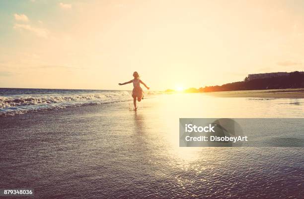 Happy Little Girl Running Inside Water On The Beach At Sunset Kid Having Fun In Holiday Vacation Youth Lifestyle And Happiness Concept Vintage Filter Focus On Silhouette Stock Photo - Download Image Now