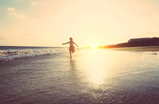 Photo of Happy little girl running inside water on the beach at sunset - Kid having fun in holiday vacation - Youth, lifestyle and happiness concept - Vintage filter - Focus on silhouette