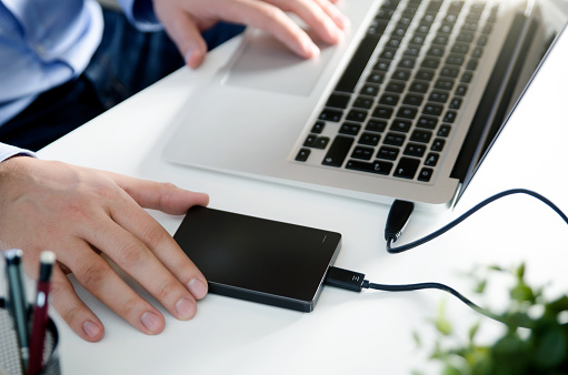 External backup disk hard drive connected to laptop. Man with notebook making safety personal data copy.