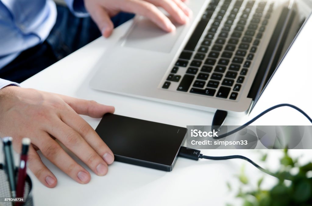 External backup disk hard drive connected to laptop External backup disk hard drive connected to laptop. Man with notebook making safety personal data copy. Hard Drive Stock Photo