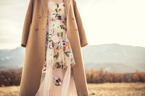 Young woman in a romantic dress and a coat enjoying in the field