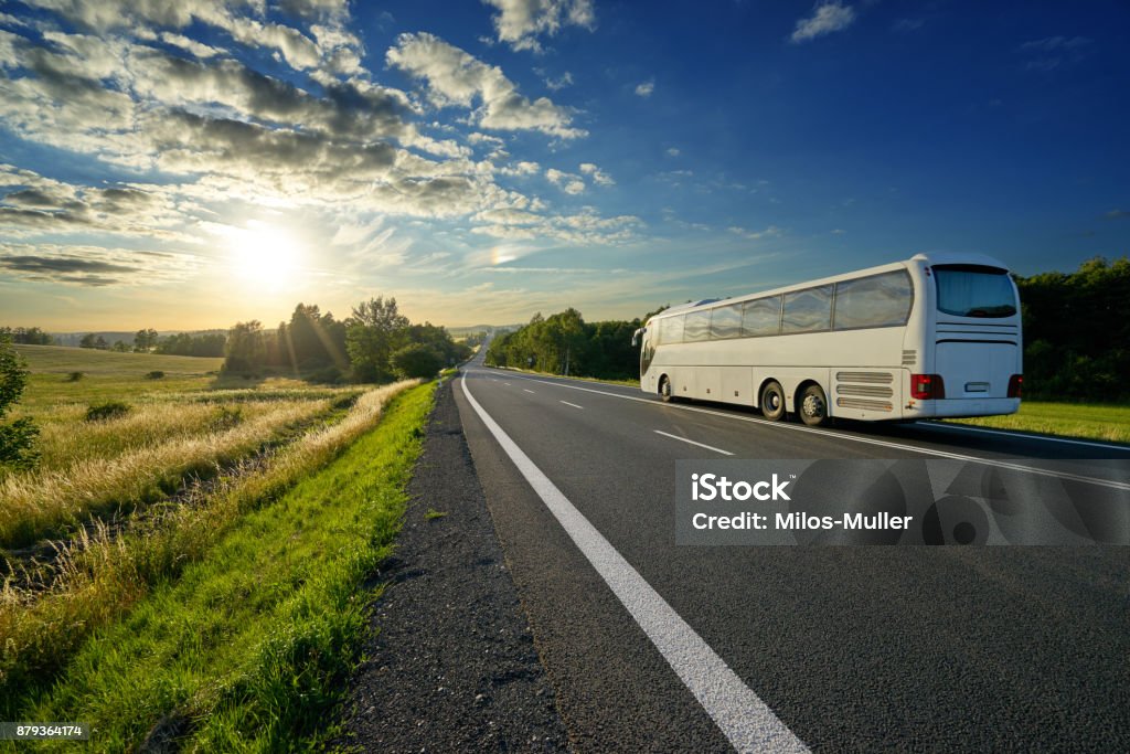 Bus blanc, voyageant sur la route asphaltée dans un paysage rural au coucher du soleil - Photo de Bus touristique libre de droits