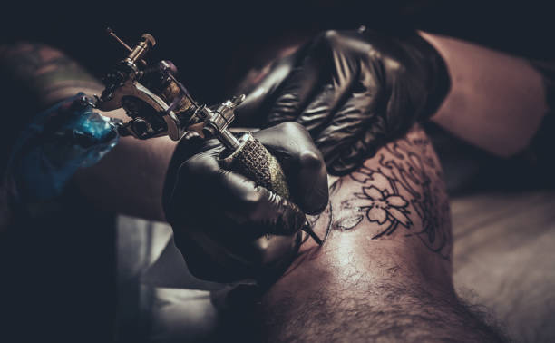 maestro del tatuaggio che fa tatuaggio sulla gamba del cliente - tatuare foto e immagini stock