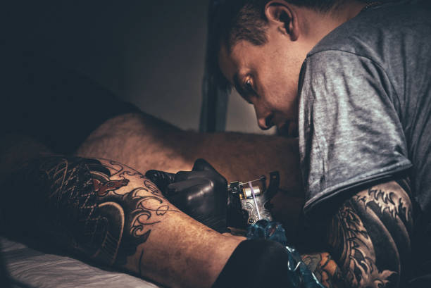 istock Tattoo master making tattoo on customer's leg 879383326