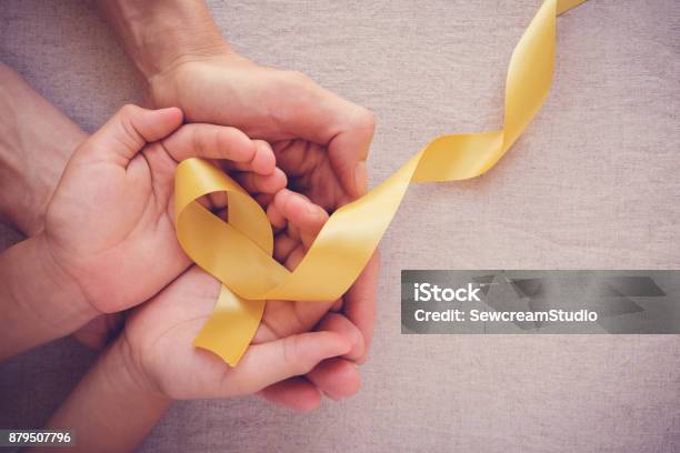 Manos De Adulto Y El Niño Con Cáncer De Hueso Amarillo Cinta Dorada Conciencia Del Sarcoma Conciencia Sobre El Cáncer Infantil Foto de stock y más banco de imágenes de Cáncer - Tumor