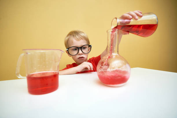 istock Small schoolboy pouring red reagent into a flask 879562310