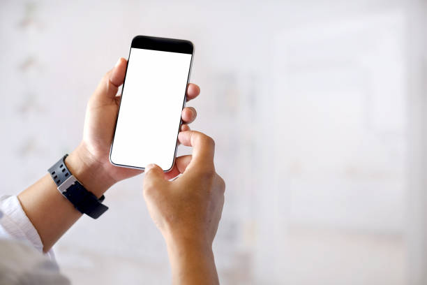 istock Mockup image of hands holding black mobile phone with blank white screen in office. 879573388
