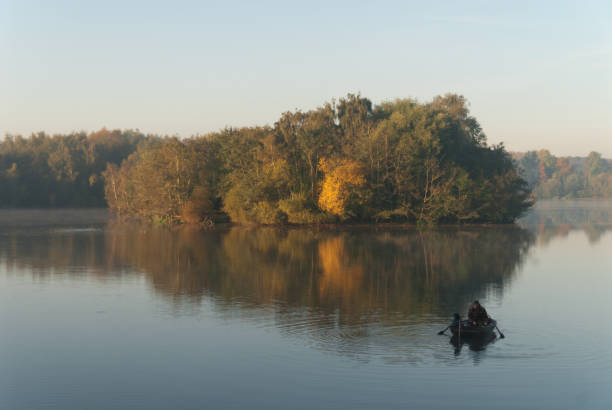Jülich, Germany - October 18, 2017: Fisherman on Barmener See with water reflections of colorful trees in autumn