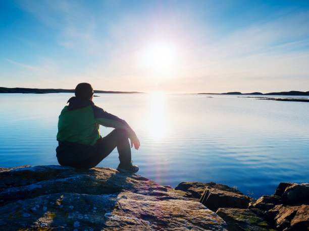 istock Man sit at evening sea. Hiker with backpack sit in squatting position  along beach. 879598620