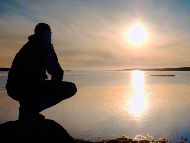 istock Man sit at evening sea. Hiker with backpack sit in squatting position  along beach. 879598764