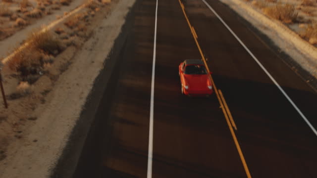 Aerial View Red Classic Car Driving Along Desolate Desert Road At Sunset