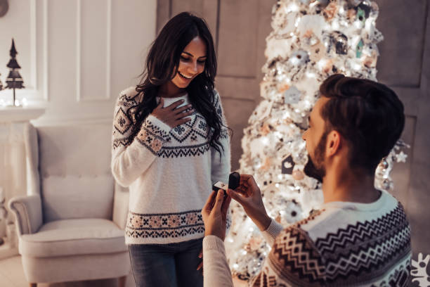 hermosa pareja está esperando el año nuevo juntos cerca de hermoso árbol de navidad en casa. - prometido fotografías e imágenes de stock