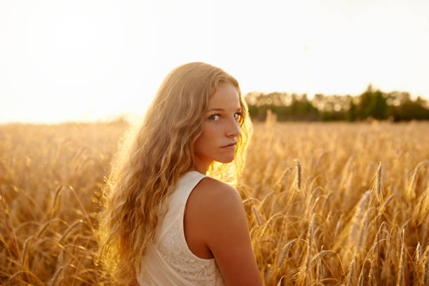 Woman in green t-shirt and white shorts stands with her back in an open field