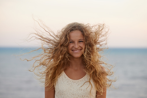 Happy pretty curly-haired woman closeup, the wind fluttering hair. Spring portrait on the beach and sea outdoors