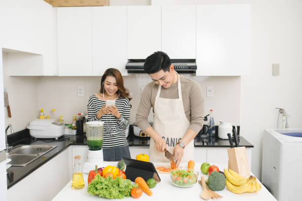 istock Asian woman using cell phone while a man prepares a meal 879641470