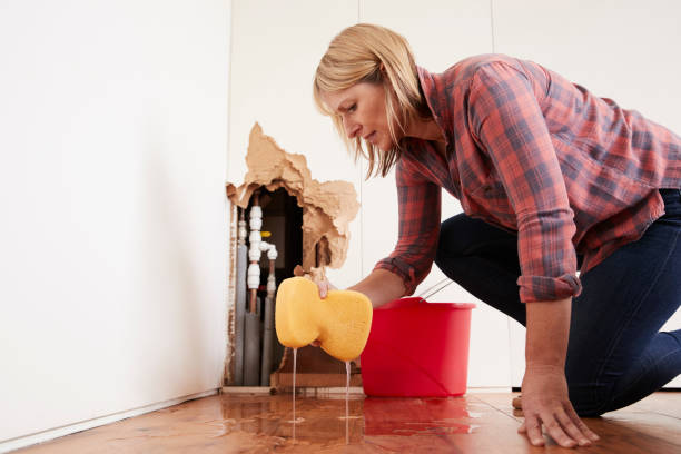 Worried woman mopping up water from a burst pipe with sponge Worried woman mopping up water from a burst pipe with sponge rolled up sleeves stock pictures, royalty-free photos & images