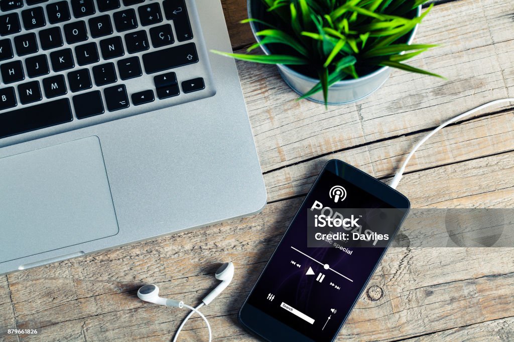 Mobile phone placed on a wooden desk with podcast app in the screen. Music and radio podcast smartphone app design placed on a mobile phone screen. Podcasting Stock Photo