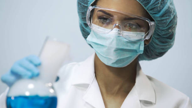 istock Female chemist holding flask with blue evaporating liquid in hand, experiment 879688934