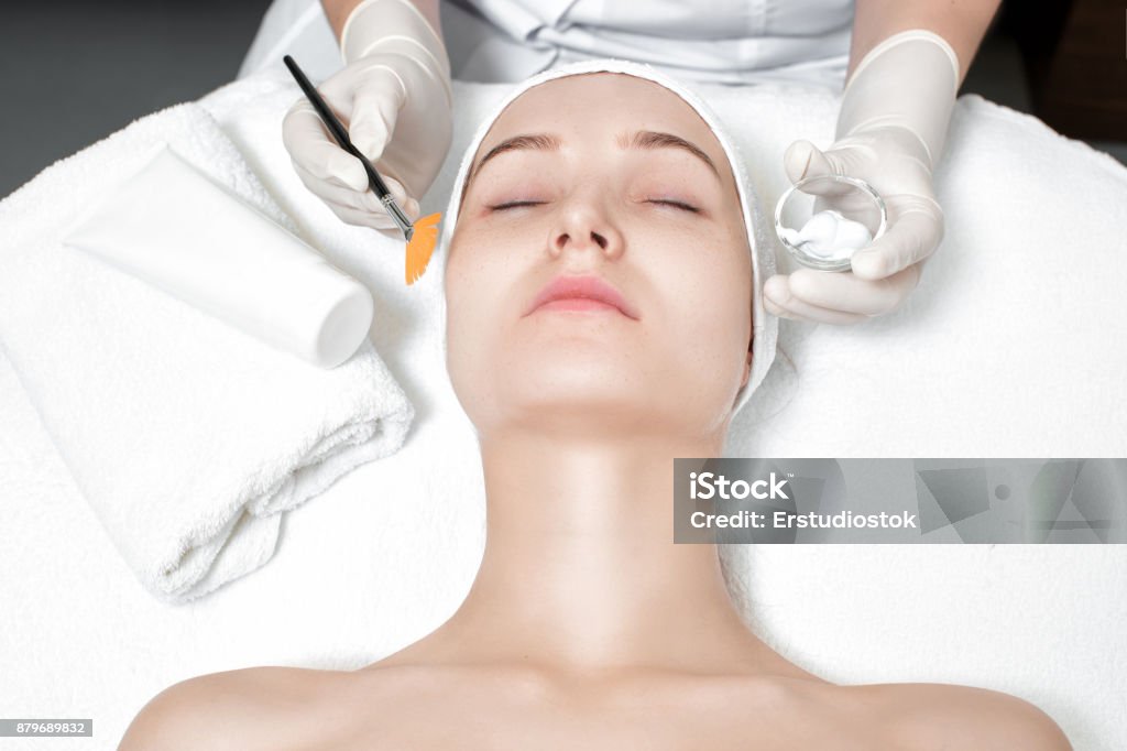 beautician applies mask to the face of  woman beautician applies the mask to the face of  beautiful young woman in the spa salon. spa treatments Peel - Plant Part Stock Photo