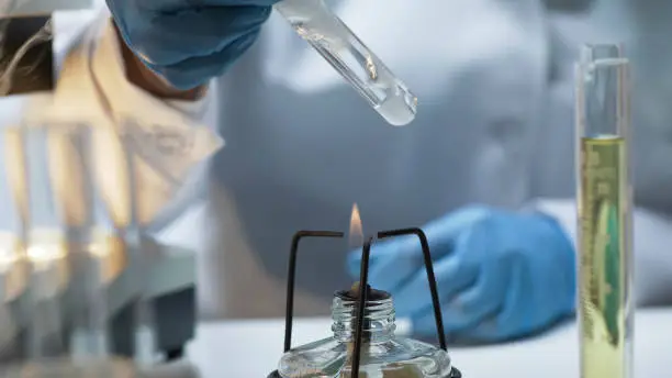 Photo of Scientist holding tube with boiling fuming liquid over burner, lab experiment