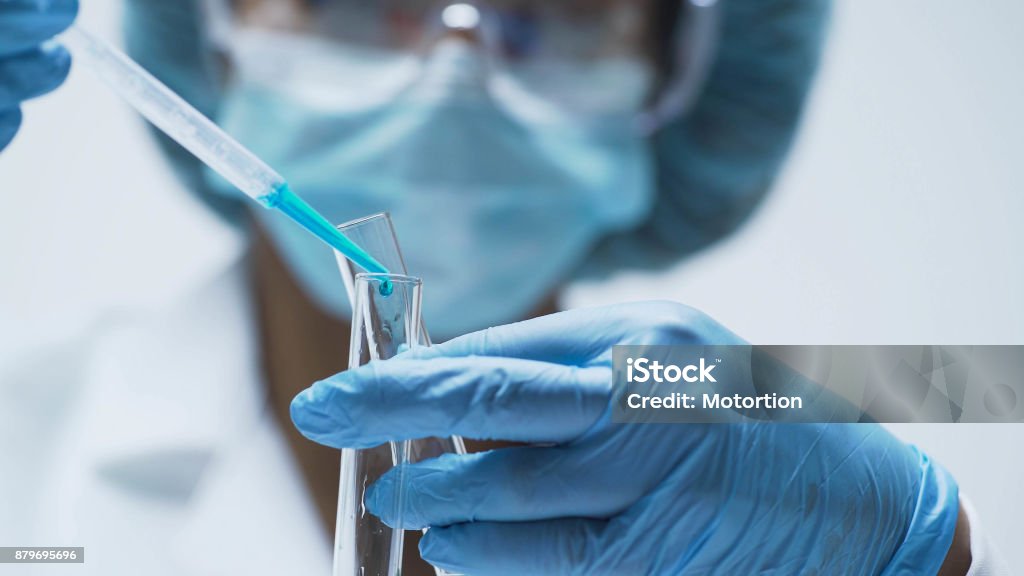 Female chemist adds drops of blue substance into test tubes, lab research Laboratory Stock Photo
