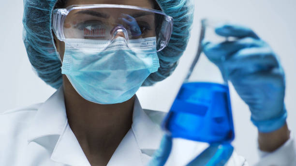 istock Attentive biracial chemist looking at conical flask with blue liquid inside 879696082