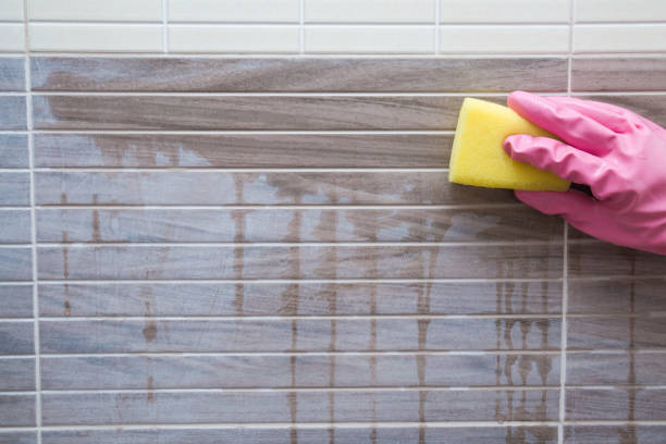 istock Employee hand in rubber protective glove with sponge washing a ceramic tiles from dust after repair in the bathroom. Before and after. Commercial cleaning company concept. 879701992