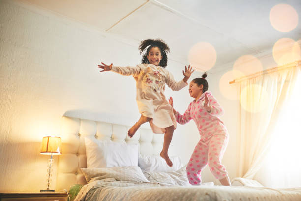 Beds are made for jumping Shot of young sisters jumping on the bed in their bedroom slumber party stock pictures, royalty-free photos & images