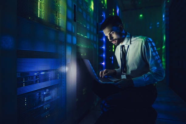 Handsome man is working in data centre with laptop. Handsome man is working in data centre with laptop.IT engineer specialist in network server room.Running diagnostics and maintenance.Technician examining server in big data center full of rack servers data cable stock pictures, royalty-free photos & images