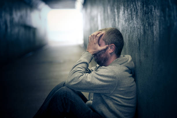 young homeless caucasian male sitting in dark subway tunnel - hopelessness imagens e fotografias de stock