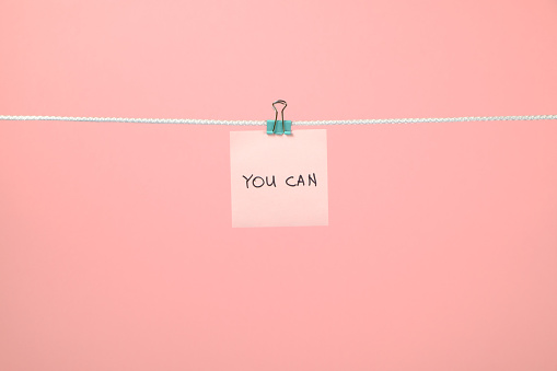 Pink paper sheet on the string with text You Can over colorful background