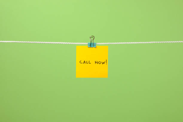 istock Yellow paper note on clothesline with text Call Now! over colorful background 879735828