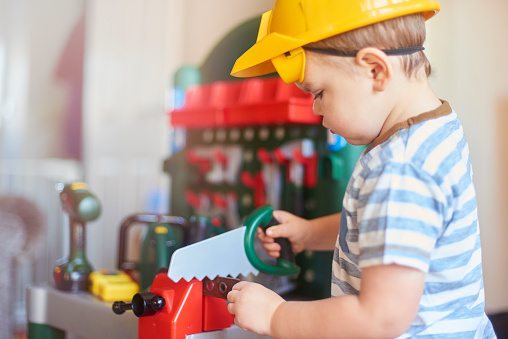 Toddler having fun dressing up as a construction worker with hard hat,goggles and construction toys