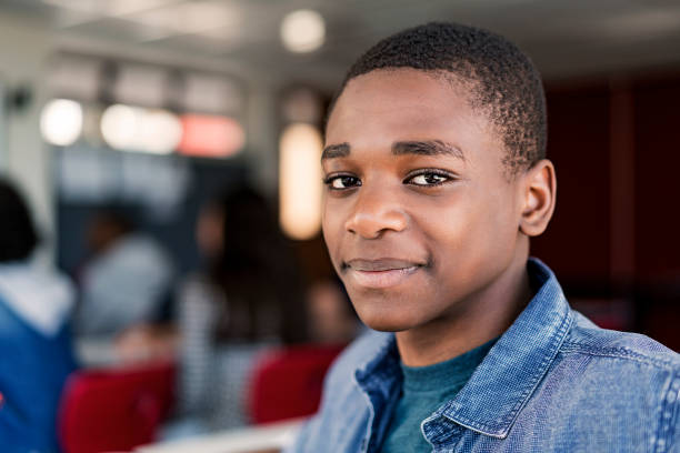 Close-up of confident male teenage student Close-up of confident teenage boy at high school. Portrait of male student is with short black hair in classroom. He is wearing blue denim. young black boys stock pictures, royalty-free photos & images