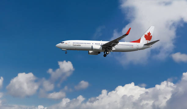 Commercial airplane with Canada flag on the tail and fuselage landing or taking off from the airport with blue cloudy sky in the background Passenger aircraft landing at the airport with flag. Blue sky with clouds in the background. Landing gear visible. boeing 737 photos stock pictures, royalty-free photos & images