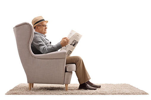 Mature man sitting in an armchair and reading a newspaper isolated on white background